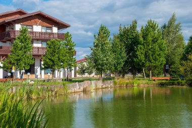 Mavi gökyüzünün ve gölün kıyısındaki ağaçların arka planında güzel bir kulübe..