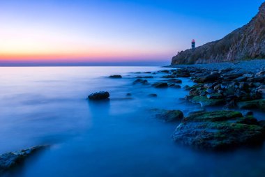 Gün batımında deniz feneri olan güzel bir deniz manzarası. Dağlar ve deniz uzun bir geçitle.