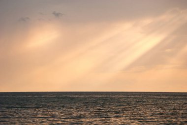 Güneş ışınları bulutların arasından denizlerin pürüzsüz sularına doğru kırılıyor..