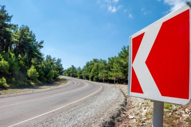 Dağ manzarası. Dağ yolu, arkadaki mavi gökyüzü ve çam ağaçlarına doğru gidiyor..