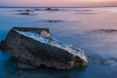 Gün batımında deniz manzarası. Taşlar ve kayalarla dolu uzun bir kepenk..