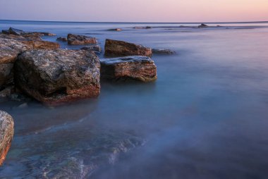 Gün batımında deniz manzarası. Taşlar ve kayalarla dolu uzun bir kepenk..