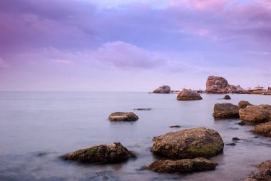 Sabah deniz manzarası. Deniz suyu uzun süre açık kalacak, taşlar ve kayalar. Bulutlu güzel gökyüzü.