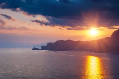 Sudak, Kırım - Cape Meganom 'un manzarası. Güzel bulutlu gün batımı gökyüzü. Karadeniz ve Kırım dağlarının sırtı akşam güneşinin altında..