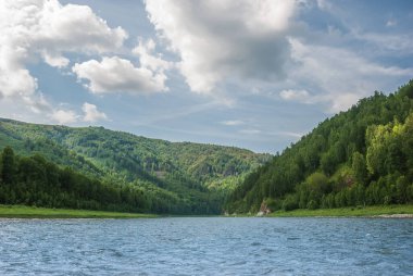 Sibirya 'nın manzarası. Kiya Nehri, dağ kıyıları ve Kemerovo bölgesindeki yeşil ormanlar. Mavi gökyüzü ve bulutlu gündüz manzarası.