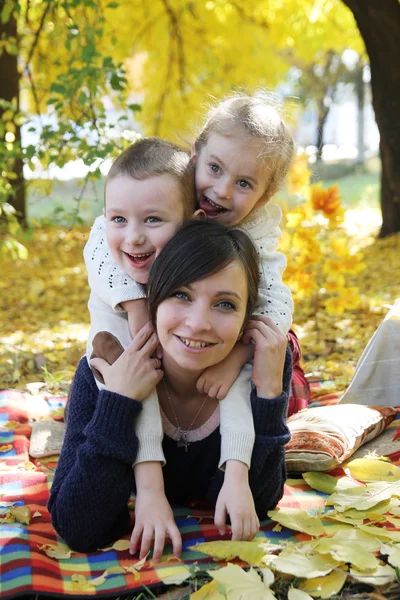 Mãe e duas crianças deitadas sob árvores de outono — Fotografia de Stock