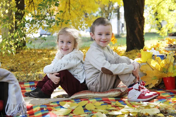 Zus en broer rug aan rug zitten onder herfst boom — Stockfoto