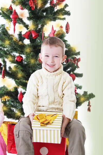 Niño sonriente con regalo bajo el árbol de Navidad —  Fotos de Stock