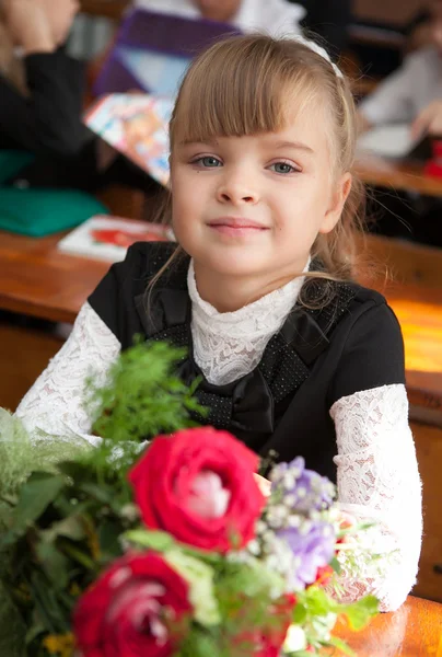 Schoolgirl at a desk with a bouquet of flowers — Stock Photo, Image