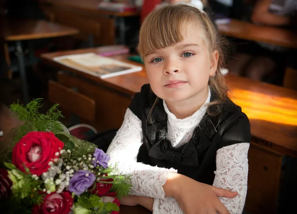 Schoolgirl at a desk with a bouquet of flowers — Stock Photo, Image