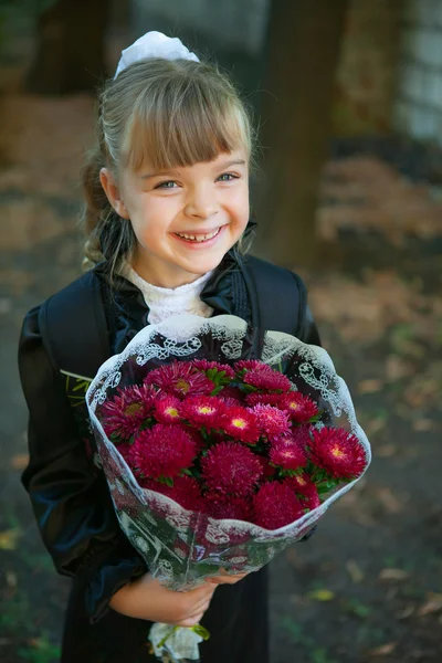 Merry skolflicka med en bukett blommor framför skola — Stockfoto