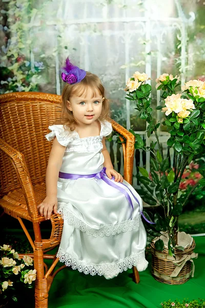 Hermosa niña en un vestido elegante en una silla de mimbre — Foto de Stock