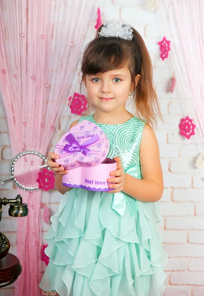 Pequena menina bonito em um vestido verde segurando um presente no cenário — Fotografia de Stock