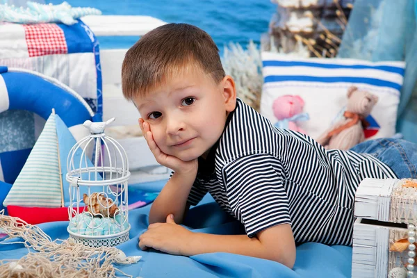 Um menino em um colete listrado encontra-se no cenário marinho — Fotografia de Stock