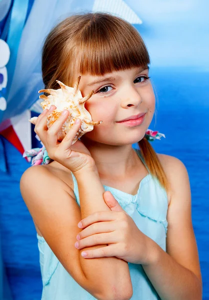 The girl in a blue dress leaning against the ear shell backgroun — Stock Photo, Image
