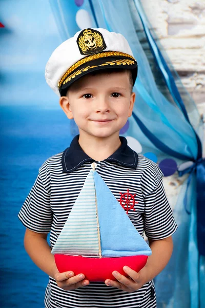 Маленький мальчик в полосатой рубашке с игрушечной лодкой на морских пейзажах — стоковое фото