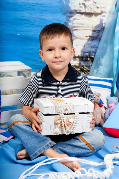 Malý chlapec v pruhovaném tričku s krabicí pokladů v moři — Stock fotografie