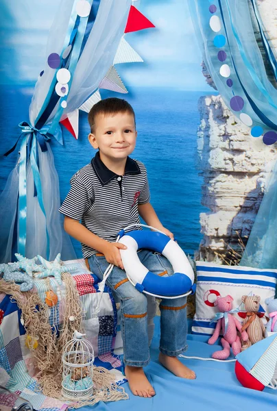 Un petit garçon en chemise rayée avec une bouée de sauvetage dans la scène maritime — Photo