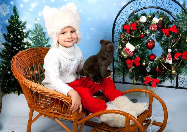 Милейший мальчик в белой меховой шляпе с медведем на новогоднем бэкгру — стоковое фото