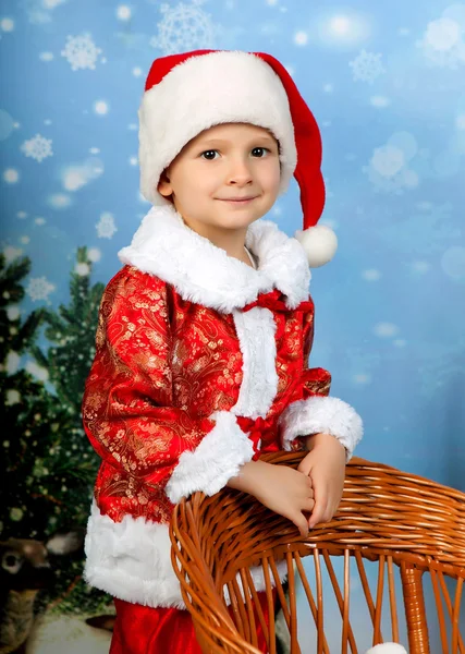 Menino bonito em um terno vermelho e boné na decoração de Natal Fotos De Bancos De Imagens Sem Royalties