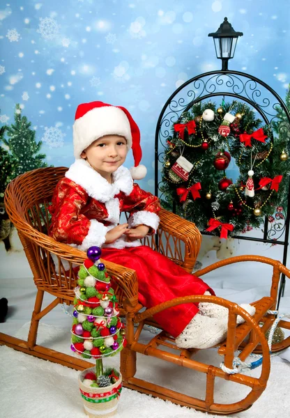 Menino bonito em um terno vermelho e boné na decoração de Natal Fotografia De Stock