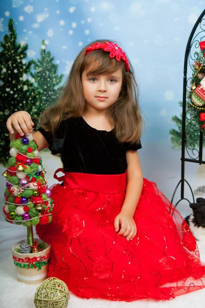 Menina bonita em um vestido vermelho e preto sentado no backgroun Fotos De Bancos De Imagens