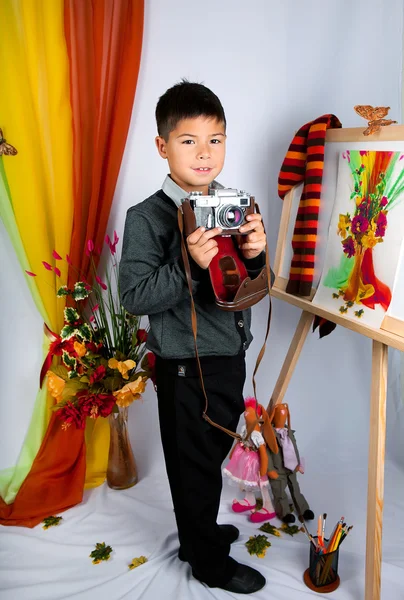 A little boy holding a vintage camera costs around easel — Stock Photo, Image