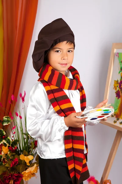 A little boy in a striped scarf and beret painting a picture on — Stock Photo, Image