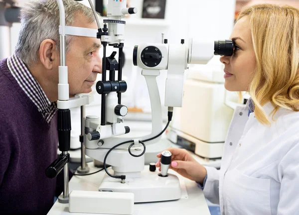 Médico oftalmológico femenino revisa ojos a anciano en clínica oftalmológica — Foto de Stock