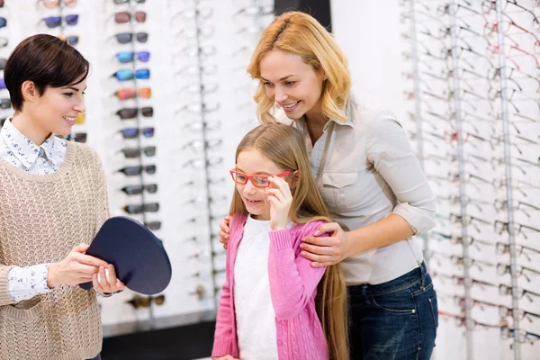 Verkäuferin hält Spiegel, während Kind Brillengestelle ausprobiert — Stockfoto