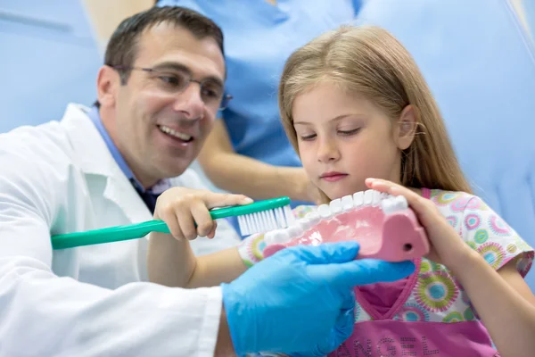 Dentista ensinando menina como escovar corretamente os dentes — Fotografia de Stock