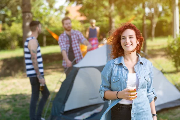 Menina encaracolado alegre com copo de cerveja de pé no acampamento de verão i — Fotografia de Stock