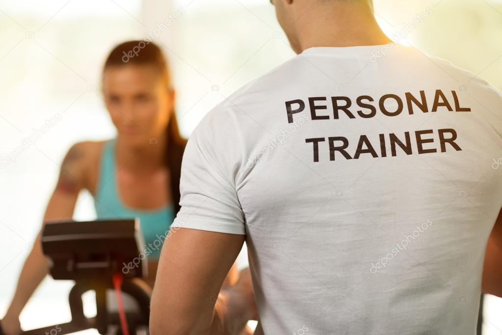 Personal trainer with woman on cycling machine at the gym 