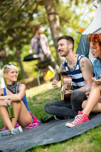 Guy tocar guitarra e meninas goza na frente da tenda no acampamento — Fotografia de Stock