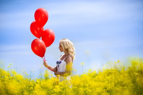 Frau in gelber Wiese mit Luftballons — Stockfoto