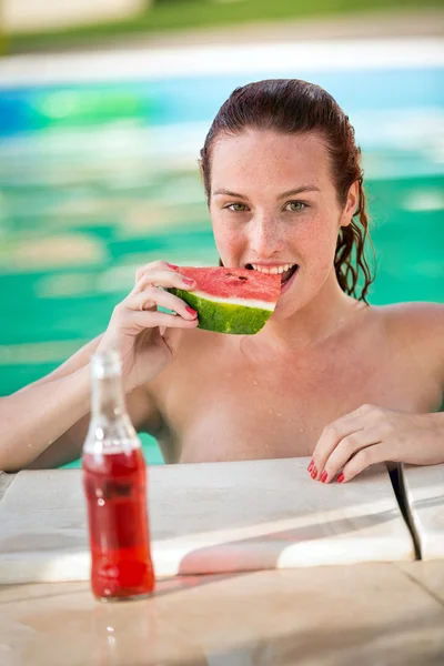 Mujer joven comiendo pedazo de sandía en la piscina —  Fotos de Stock