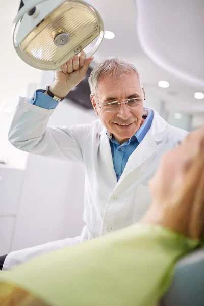 Dentist adjust searchlight to illumine patient's mouth — Stock Photo, Image