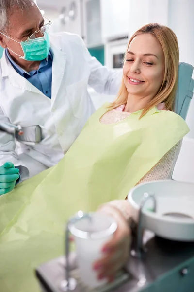 Paciente feminina em cadeira odontológica toma copo de água — Fotografia de Stock