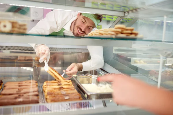 Vendor in bakery taking out biscuit with cream from showcase — Stock Photo, Image