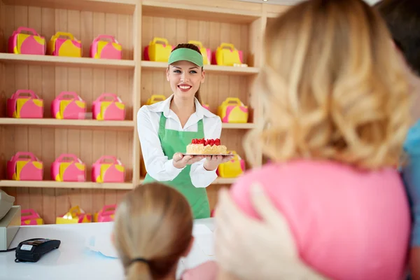 Shopkeeper gives cakes with strawberry to young family — Stock Photo, Image