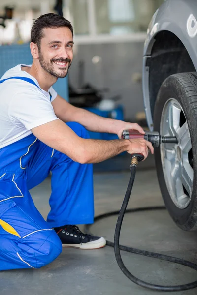 Mecánico sonriente cambiando neumático en el coche —  Fotos de Stock