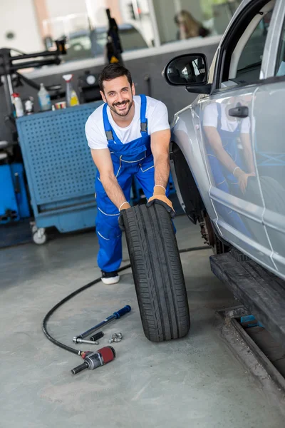 Uśmiechający się mechanik naprawy i przesuwając czarny opona — Zdjęcie stockowe