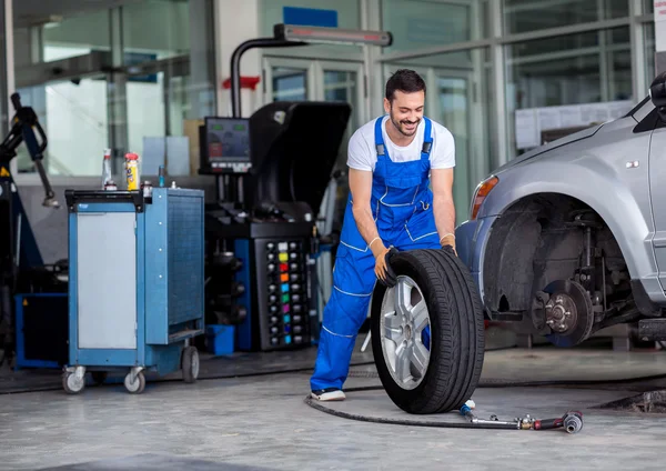 Smiling mechanic pushes the tire — Stock Photo, Image