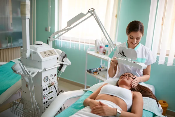 Jovencita alegre está recibiendo tratamiento facial por esteticista —  Fotos de Stock