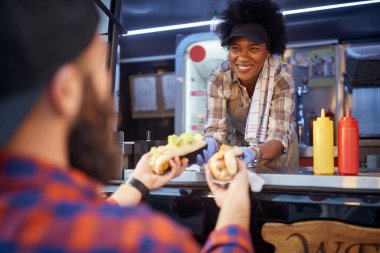 Nazik Afro-Amerikalı kadın çalışan, sakallı beyaz bir erkek müşteriye iki sandviç veriyor. Fast food servisi