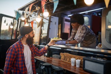 Genç sakallı hippi, fast food servisindeki kibar bayan çalışandan sandviç alıyor.