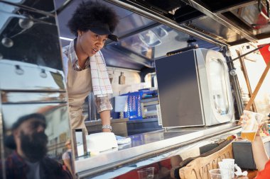 Fast food servisindeki genç Afro-Amerikan bayan çalışanı şapkalı genç beyaz sakallı hippiye baktığını yazıyor. Yansıma.