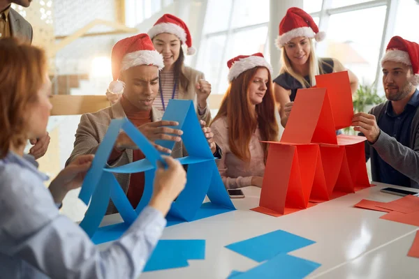 blue and red team of employees competing in building card towers at the office for christmas