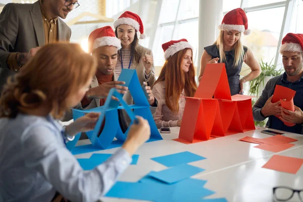 サンタ ハットとビルカードタワーで競い合うオフィスの人たち クリスマスタイム — ストック写真