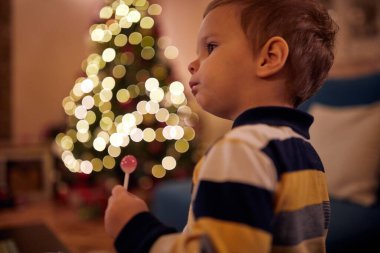 Küçük bir çocuk Noel arifesinde evde lolipopun tadını çıkarıyor. Birlikte, yeni yıl, aile, kutlama